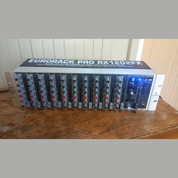 Stříbrný rackový mixážní pult s černým předním panelem. Na horní části je nápis EURORACK PRO RX1202FX a pod ním text ULTRA LOW-NOISE DESIGN 12-INP. M…