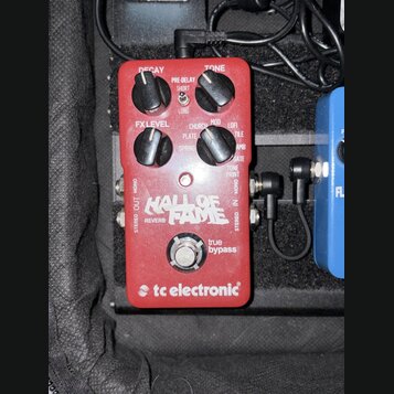 Červený kytarový efekt s nápisy HALL OF FAME REVERB a tc electronic. Na horní straně jsou čtyři černé ovládací knoflíky s popisky DECAY, PRE-DELAY, T…