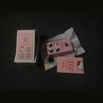 Růžový efekt pedál s nápisem FUZZ a logem Fender. Na pedálu je grafika postavy Hello Kitty a tři ovládací knoflíky. Součástí je originální krabice s…
