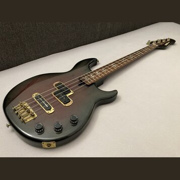 Elektrická basová kytara s tmavým, přechodovým lakem od červené po černou. Na hmatníku jsou vidět čtyři vložky s nápisem "YAMAHA". Nástroj má zlatý h…