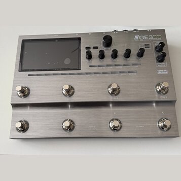 Stříbrný efektový procesor s kovovým povrchem a displejem. Na horním panelu je nápis GE3CC Amp modeling & Multi effects, dále označení EXP1, EXP2, XL…