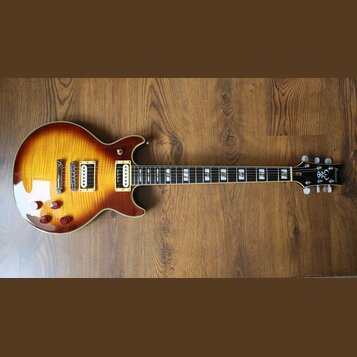 Elektrická kytara s tvarem singlecut a povrchovou úpravou sunburst v žlutých a hnědých tónech. Na hlavě je viditelné logo s nápisem Ibanez. Nástroj m…