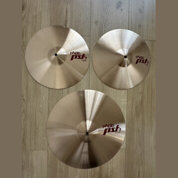 Tři mosazné činely s viditelným broušením povrchu položené na dřevěné podlaze. Všechny tři mají červenobílé logo pAiste pst 1. Činely mají nápisy 14"…