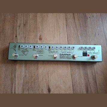 Stříbrný efektový pedalboard s nápisem DAPPER INDIE. Obsahuje pět sekcí s ovládacími knoflíky a přepínači, které jsou označeny názvy AMBIENT, ECHOES,…