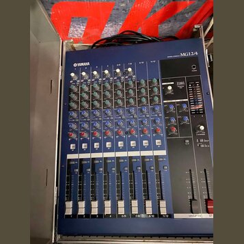 Modrý mixovací pult s nápisem MIXING CONSOLE MG12/4 a logem YAMAHA. Zařízení obsahuje několik vstupních kanálů s ovládacími knoflíky a posuvníky. Pov…
