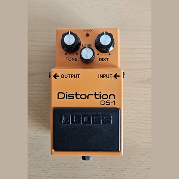 Kytarový efekt v oranžovém provedení s černým spínacím pedálem. Na šasi jsou nápisy Distortion, DS-1 a na pedálu logo BOSS. Horní část obsahuje tři o…