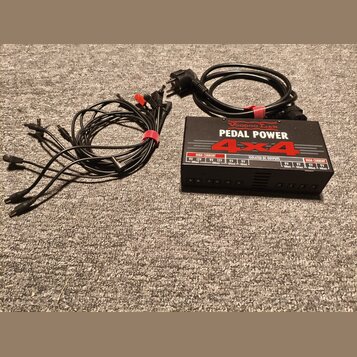 Černý napájecí adaptér Voodoo Lab PEDAL POWER 4x4 s nápisy HIGH CURRENT a ISOLATED DC OUTPUTS. K zařízení patří napájecí kabel do zásuvky a sada čern…