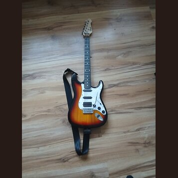 Elektrická kytara s trupem v přechodovém žlutě-černém odstínu (sunburst) a bílým pickguardem. Na hlavě hmatníku je viditelné logo Fender. Kytara má t…