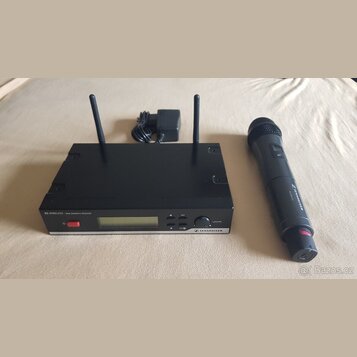 Černý bezdrátový přijímač s dvěma anténami a doprovodný černý bezdrátový mikrofon. Na předním panelu přijímače je nápis XS WIRELESS TRUE DIVERSITY RE…