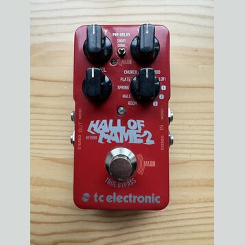 Červený kytarový efekt s nápisem HALL OF FAME 2 a logem tc electronic. Na horní části jsou čtyři černé ovládací knoflíky a nápisy PRE-DELAY (SHORT, L…