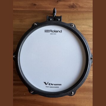 Elektronický buben s bílým pleteným povrchem a černým obručováním. Na horní části je nápis Roland MESH HEAD a v dolní části V-Drums s doplňkem Patent…