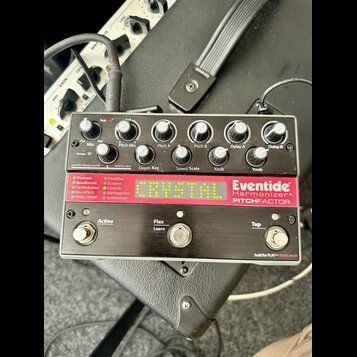 Kytarový efekt pedál značky Eventide s nápisy Harmonizer® a PITCHFACTOR. Zařízení má stříbrný kovový korpus, pět černých otočných oválů a dvě stoupac…