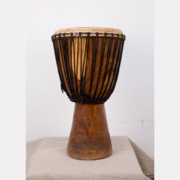 Djembe s dřevěným korpusem v přirozené hnědé barvě. Horní část je obvolta opletena černými provazy, které drží napnutou koženou membránu. Spodní část…