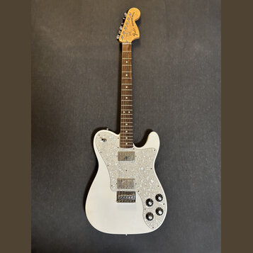 Bílá elektrická kytara s hnědým hmatníkem a perleťovým pickguardem. Na hlavě je viditelné logo Fender a nápis Telecaster Deluxe. Nástroj vykazuje zná…