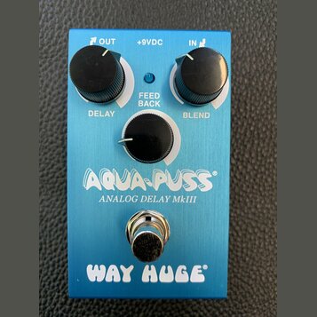 Modrý kytarový efekt s nápisy AQUA-PUSS, ANALOG DELAY MkIII a WAY HUGE. Na horní straně jsou tři černé otočné knoflíky s popisky DELAY, FEED BACK a B…