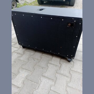 Černý obdélníkový reproduktorový box s povrchem z textilie. Na zadní straně je umístěn jeden konektor pro kabel a v horní části horního panelu je výř…