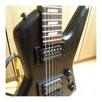 Černá elektrická kytara s tmavým hmatníkem a bílými vložkami. Nástroj má dva černý humbuckery a dva ovládací knofíky. Kytara je umístěna v žlutém sto…
