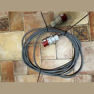 Šedý silový kabel smouseDowným červeným konektorem a zásuvkou. Na bílém plastovém krytu konektoru jsou nečitelné nápisy. Kabel je svázaný černými pla…
