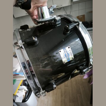 Černý buben s chromovanými obručmi a ladicími šrouby. Na korpusu je viditelný bílo-modrý štítek s nápisy YAMAHA, Stage Custom a MADE IN JAPAN. Povrch…