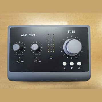 Šedý audio rozhraní s nápisy AUDIENT a iD14. Zařízení má velký ovládací knoflík, dva menší knoflíky s označením GAIN 0 10 u kanálů 1 a 2, dva přepína…