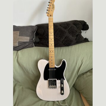 Bílá elektrická kytara typu Telecaster se světle hnědým hmatníkem a černým pickguardem. Na hlavě je viditelné logo Squier. Nástroj vykazuje známky bě…