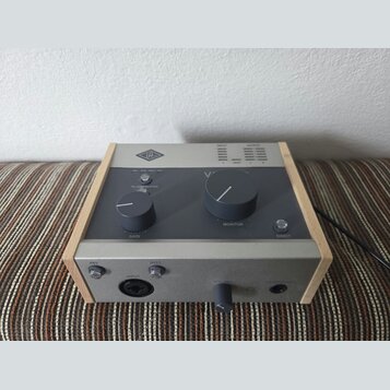 Šedý audio procesor v dřevěném rámu. Na horním panelu je logo UA, nápisy INPUT a OUTPUT s LED indikátory, přepínač s označením VOC, GTR, FAST, OFF a…