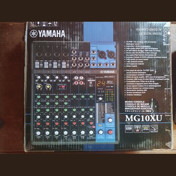 Fotografie zobrazuje míchací pult Yamaha MG10XU v původním kartónovém obalu. Na přístroji je viditelné logo YAMAHA a označení modelu MIXING CONSOLE M…
