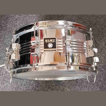 Chromovaný malý buben s kovovým korpusem. Uprostřed je černý štítek s bílým nápisem MAPEX PERCUSSION TECHNOLOGY a pod ním menší text MADE IN TAIWAN R…