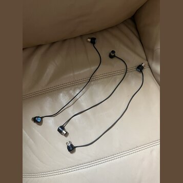 Tři černé audio kabely s konektory na obou koncích. Na některých konektorech jsou vidět modré značky s bílým textem, který je nečitelný. Kabely leží…