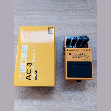 Žlutý efekt pedál Boss Acoustic Simulator AC-3 v originální žluté krabici. Na pedálu jsou tři ovládací knoflíky, červená kontrolka s nápisem CHECK a…