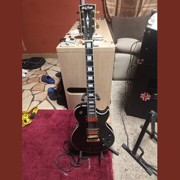 Černá elektrická kytara s tvarem single-cutaway, zlatým hardwarem a hnědým hрифem. Na hlavě je bílý nápis Harley Benton a pod ním značka HB. Kytara m…