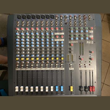 Šedý mixovací pult s vícevstupovými kanály a posuvníky. Na horní části je vidět nápis ALLEN&HEATH a označení modelu PA12. Zařízení obsahuje řadu bare…