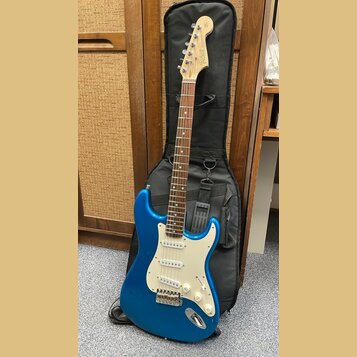Modrá elektrická kytara s bílým pickguardem a hnědým hmatníkem, opřená o černý pouzdro. Na hlavě kytary je viditelné logo Telecaster. Nástroj má tři…