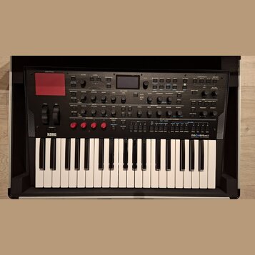 Černý klávesový syntetizátor s bílými klávesami. Na levé straně je logo KORG a na pravé nápis modwave mkII WAVE TABLE SYNTHESIZER. Horní panel obsahu…