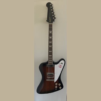 Elektrická kytara s tmavě hnědým gradientním lakem a bílým plechtrátem. Na hlavě je zlatý nápis Epiphone a na plechtrátu se nachází červené logo. Nás…