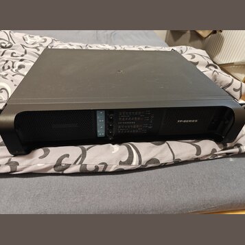 Černý výkonový zesilovač v kovovém šasi s ochrannými úhly. Na předním panelu je nápis FP-SERIES a označení modelu FP10000Q. Jsou zde vidět ovládací p…