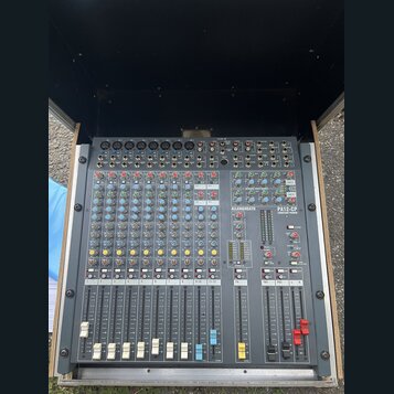 Šedý mixážní pult umístěný v transportním kufru. Na přístroji je vidět bílý nápis ALLEN&HEATH a označení modelu PA12-CP CONSTANT POWER. Povrch pultu…