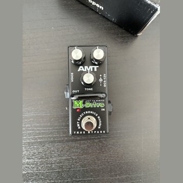 Černý efekt pedál s třemi bílými ovládacími knoflíky. Na horní části je bílé logo AMT a popisky VOICE, TONE a DC9-12V. Spodní část obsahuje zelený ná…