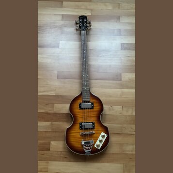 Čtyřstrunná basová kytara s tělem ve tvaru houslí a barevným přechodem od žluté k tmavě hnědé. Na hlavě je viditelné logo Epiphone. Nástroj má dva sn…