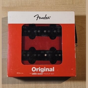 Krabice značky Fender obsahuje sadu dvou černých snímačů. Na spodní části červeného obalu je bílý nápis Original a JAZZ BASS PICKUP SET. Papírové bal…