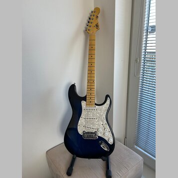 Elektrická kytara s tmavě modrým přechodovým lakem a bílým perleťovým pickguardem. Na hlavě hmatníku je viditelné logo Squier. Krk a hmatník jsou vyr…