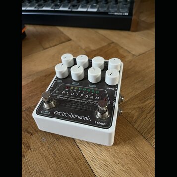 Bílý efekt pedál s osmi bílými oválnými ovladači. Na horním panelu je nápis PLATFORM a pod ním text stereo compressor/limiter. Ve spodní části je log…
