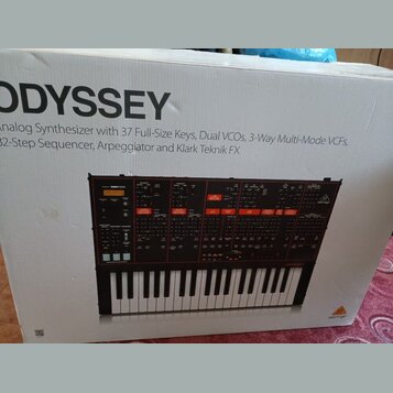 Fotografie zachycuje kartonovou krabici s obrázkem analogového syntetizátoru. Na krabici je velký nápis ODYSSEY a text Analog Synthesizer with 37 Ful…