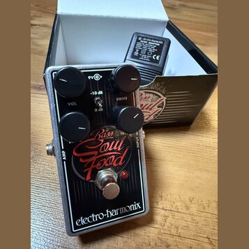 Černý efekt pedál s bílým lemováním a nápisy Bass Soul Food a electro-harmonix. Na horní části jsou čtyři černé ovládací knoflíky a přepínač s označe…