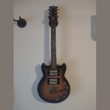 Elektrická kytara s tmavě hnědým gradientem (sunburst) a hnedým hmatníkem. Na hlavě je viditelné logo Epiphone. Nástroj má dva humbuckery, tři ovláda…