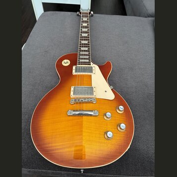 Elektrická kytara s trupem v barvě sunburst a viditnou strukturou dřeva. Nástroj má dva humbuckery, bílý plechtrpáč a čtyři zlaté ovládací knoflíky.…