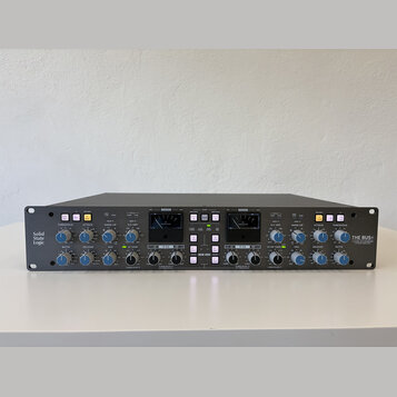 Šedý rackový studiový kompresor s nápisy Solid State Logic vlevo a THE BUS+ vpravo. Přední panel obsahuje dva analogové VU metry, řadu regulačních kn…