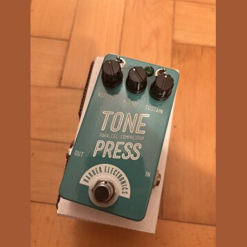 Tyrkysový efekt pedál s bílými nápisy. Na horní straně jsou tři černé oválné knoflíky s popisky VOLUME, BLEND a SUSTAIN. Uprostřed je velký bílý nápi…