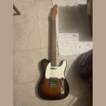 Elektrická kytara typu Telecaster s tónem sunburst (přechod od černé k hnědé a žluté). Má bílý pickguard, dva snímače a na hlavě hmatníku je viditeln…