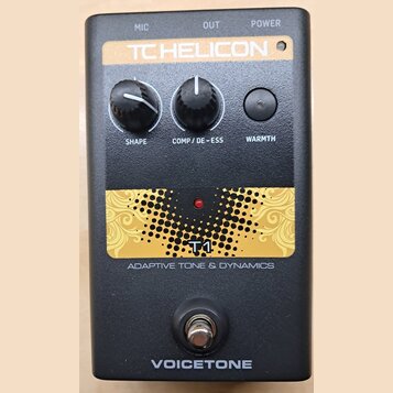 Černý efekt pedál s nápisy TC HELICON a VOICETONE. Na horní části jsou dva černé otočné ovladače s popisky SHAPE a COMP / DE-ESS a jedno tlačítko WAR…